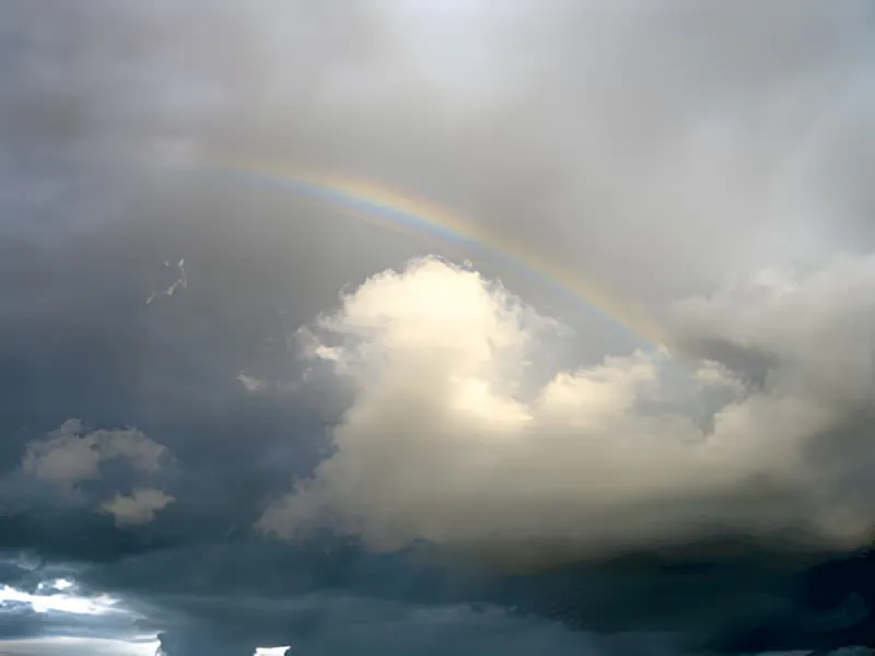 Un arc-en-ciel partiel s'arquant à travers les nuages d'orage gris au-dessus du paysage campagnard.
