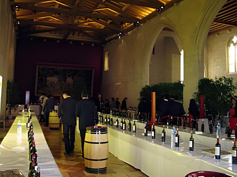 Une élégante salle voûtée en pierre avec de hauts plafonds où les gens mènent des dégustations de vin à des tables bordées de nombreuses bouteilles.