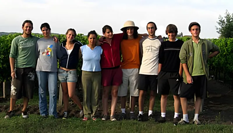 Un groupe diversifié de neuf travailleurs temporaires debout ensemble en ligne devant un vignoble au Château Plaisance, souriant pour une photo de groupe.