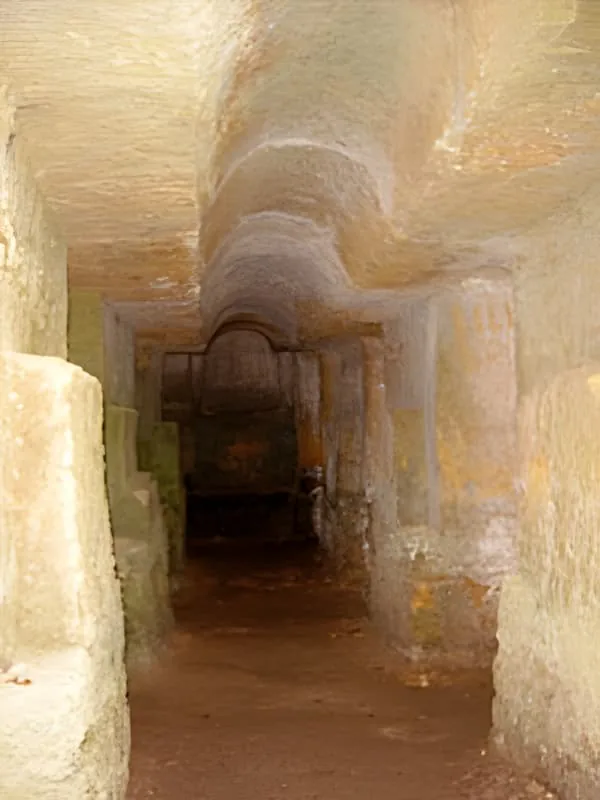 Un tunnel ou couloir en calcaire sculpté montrant les murs de couleur ocre chaude et le plafond voûté, représentant l'architecture souterraine antique.